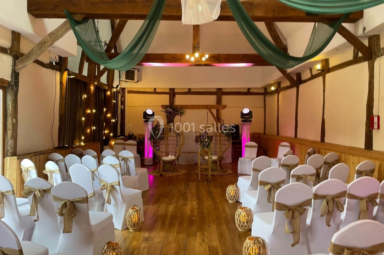 Salle de réception décorée pour un mariage, avec chaises blanches, lanternes au sol et drapés verts suspendus.
