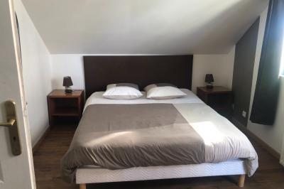 Lit double avec tête de lit sombre, draps gris et blancs, encadré par deux tables de chevet avec lampes, dans une chambre…