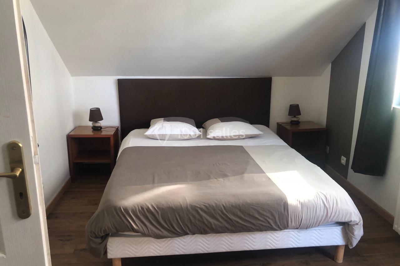 Lit double avec tête de lit sombre, draps gris et blancs, encadré par deux tables de chevet avec lampes, dans une chambre…