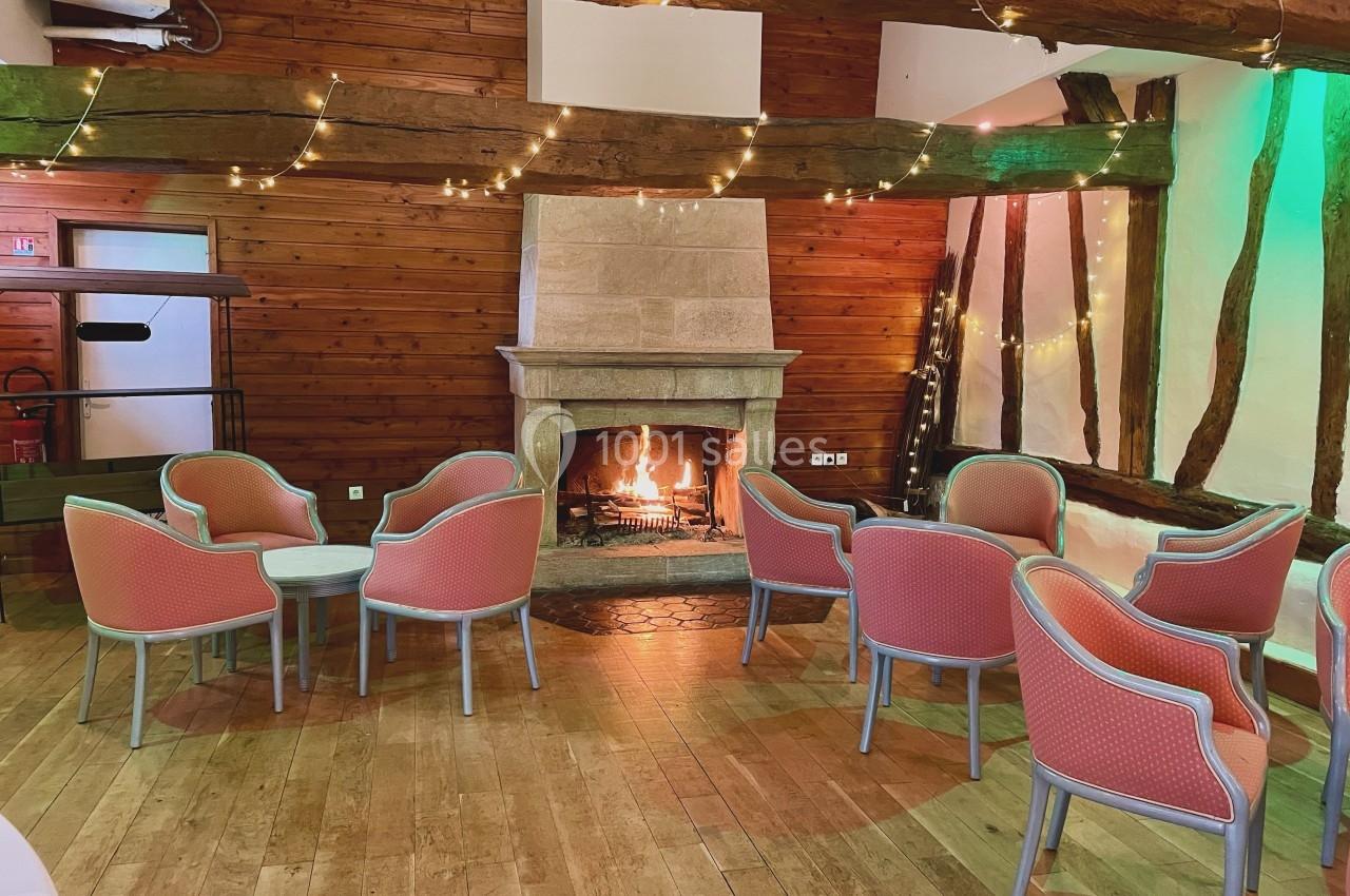 Salle chaleureuse avec cheminée allumée, chaises rembourrées roses et murs en bois ornés de guirlandes lumineuses.