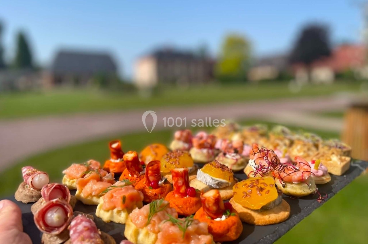 Plateau d'amuse-bouches variés présenté en extérieur, avec un jardin flou en arrière-plan.