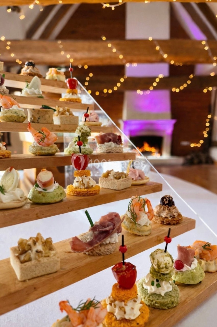 Plateau en escalier avec divers amuse-bouches colorés dans une salle décorée de guirlandes lumineuses et cheminée allumée.