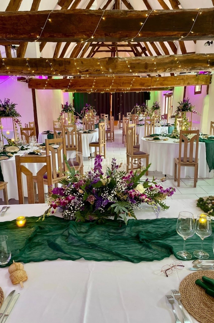 Salle de réception décorée avec des tables rondes, nappes blanches, chemins de table verts et compositions florales.