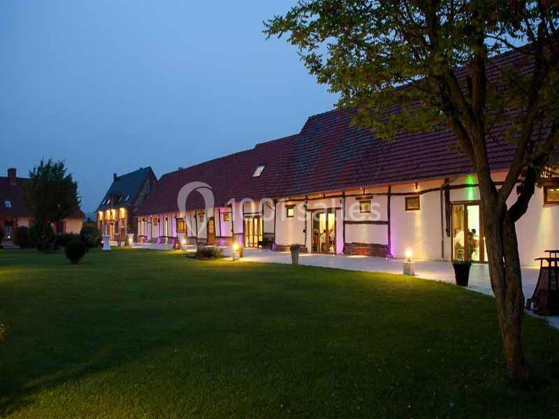 Bâtiment à colombages éclairé en soirée, entouré d'une pelouse et d'arbres.