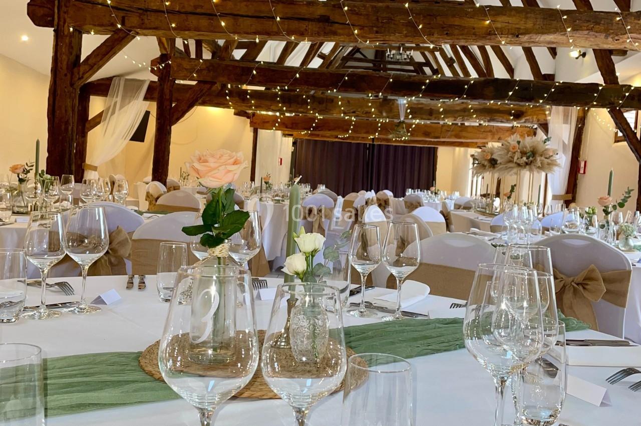 Salle de réception décorée pour un mariage avec tables dressées, nappes blanches, fleurs et guirlandes lumineuses suspendues.