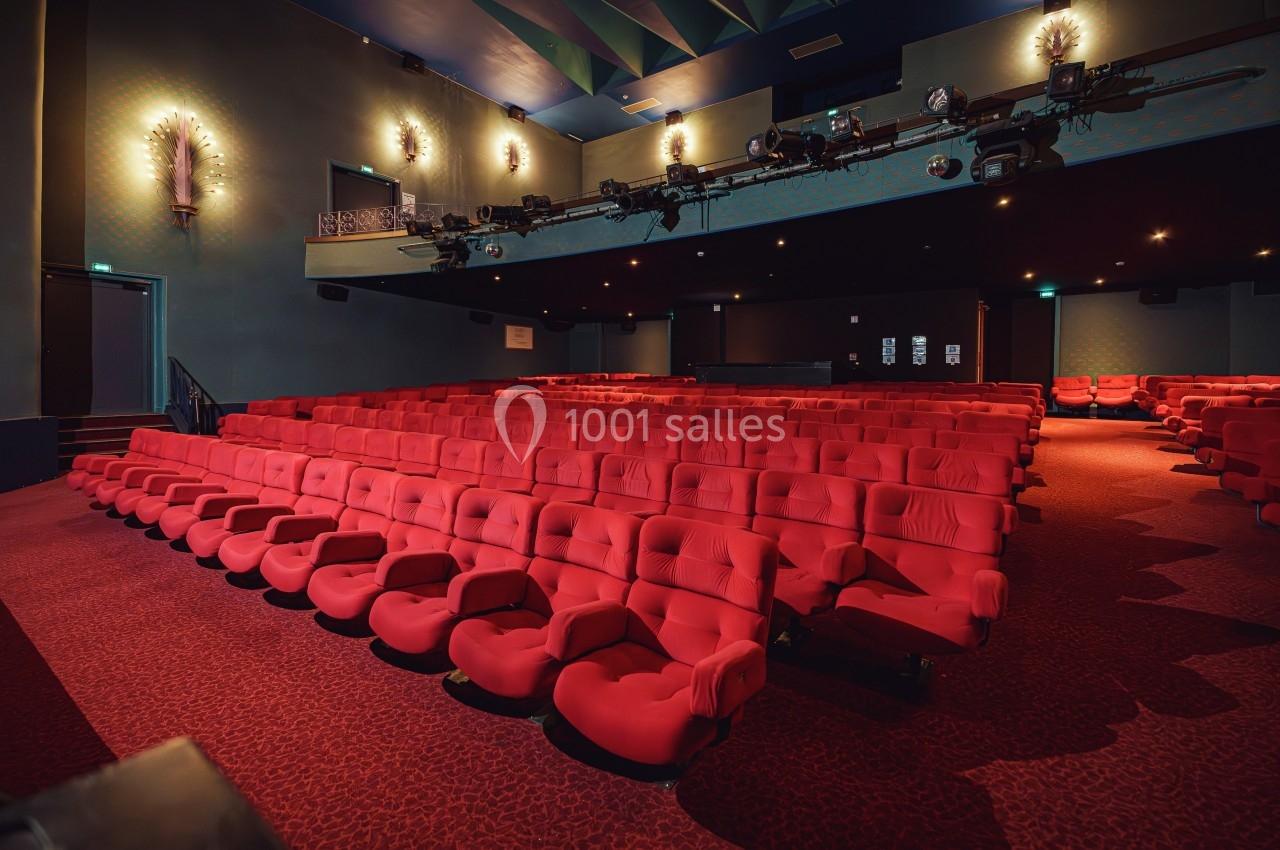 Salle de cinéma vide avec des fauteuils rouges alignés et un éclairage tamisé.