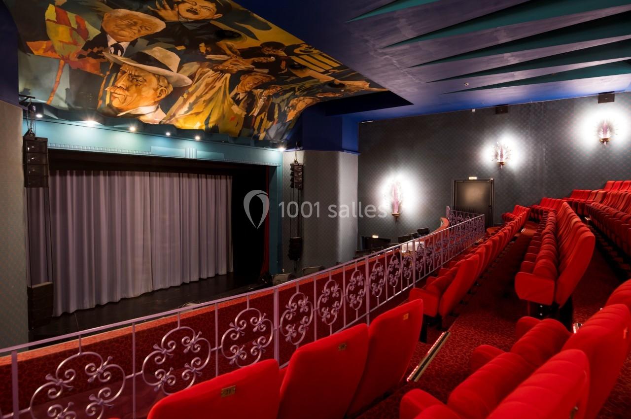 Salle de théâtre avec sièges rouges, scène avec rideau fermé et fresque colorée au plafond.