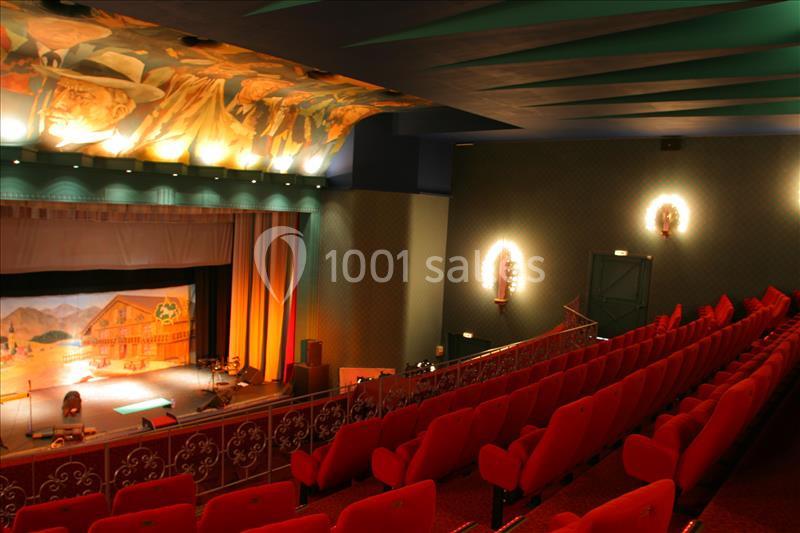 Salle de théâtre avec rangées de sièges rouges, scène éclairée et plafond décoré de fresques artistiques.