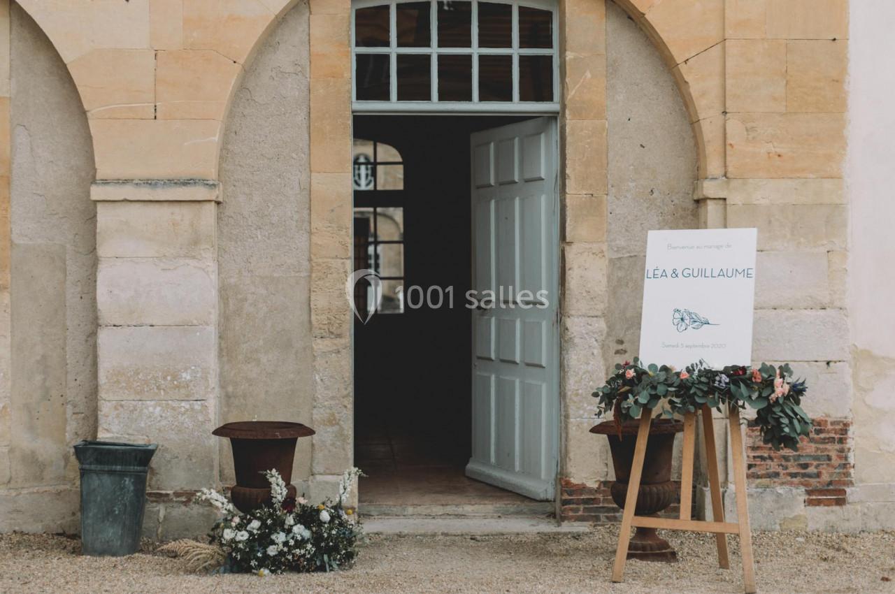 Entrée d'un bâtiment ancien avec une porte ouverte, un panneau de mariage et des décorations florales.