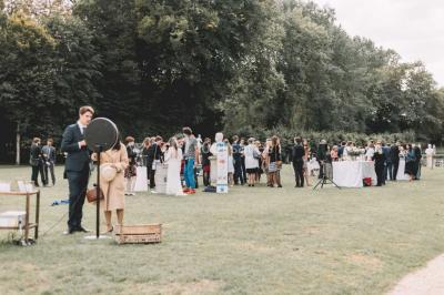 Groupe de personnes rassemblées dans un jardin près d'une bâtisse ancienne, sous une tente blanche par temps clair.