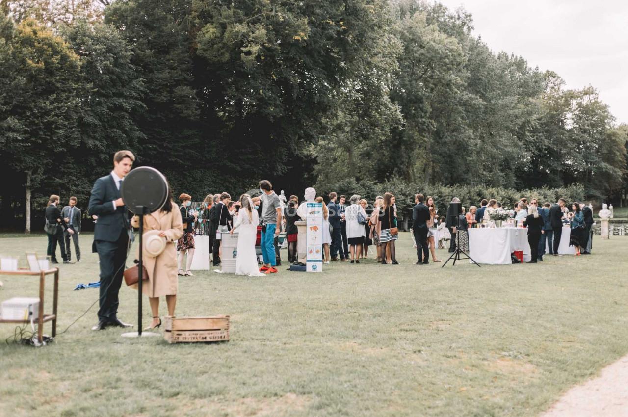 Groupe de personnes rassemblées dans un parc pour un événement, avec des stands et des tables en arrière-plan.