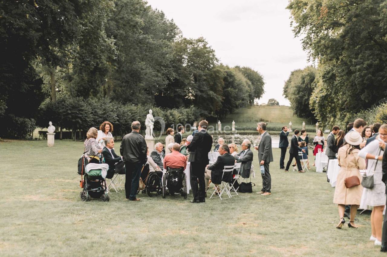Un groupe de personnes discute et se tient debout ou assis dans un parc verdoyant avec des statues en arrière-plan.