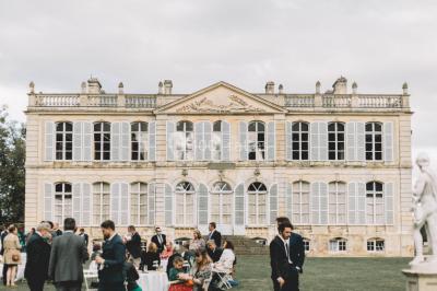 Groupe de personnes rassemblées dans un jardin près d'une bâtisse ancienne, sous une tente blanche par temps clair.