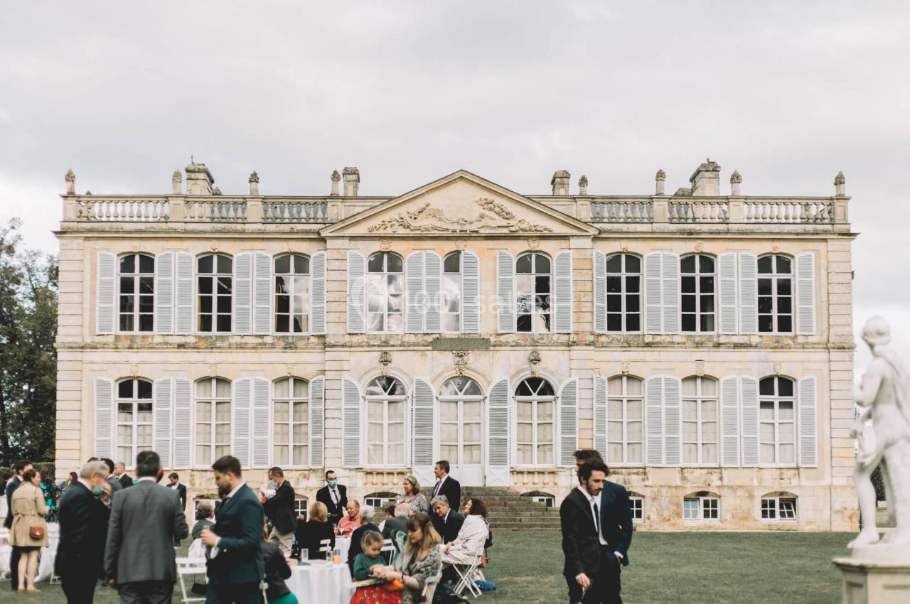 Groupe de personnes rassemblées sur une pelouse devant un grand bâtiment historique avec des fenêtres à volets.