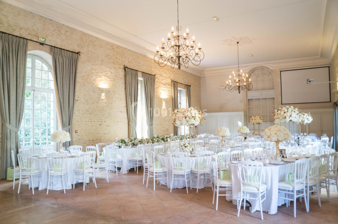 Salle de réception lumineuse avec tables rondes décorées de nappes blanches et compositions florales élégantes.
