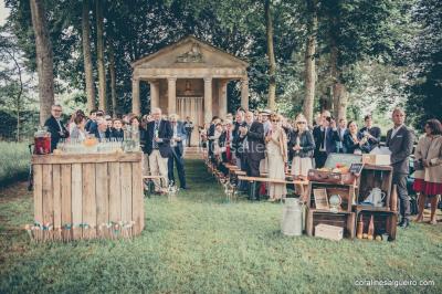 Groupe de personnes rassemblées dans un jardin près d'une bâtisse ancienne, sous une tente blanche par temps clair.