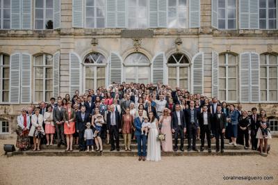 Groupe de personnes rassemblées dans un jardin près d'une bâtisse ancienne, sous une tente blanche par temps clair.