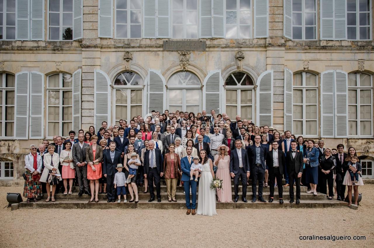 Groupe de personnes posant devant un bâtiment ancien avec des fenêtres à volets blancs.