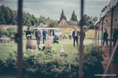 Groupe de personnes rassemblées dans un jardin près d'une bâtisse ancienne, sous une tente blanche par temps clair.