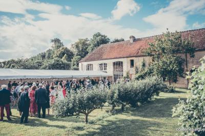 Groupe de personnes rassemblées dans un jardin près d'une bâtisse ancienne, sous une tente blanche par temps clair.