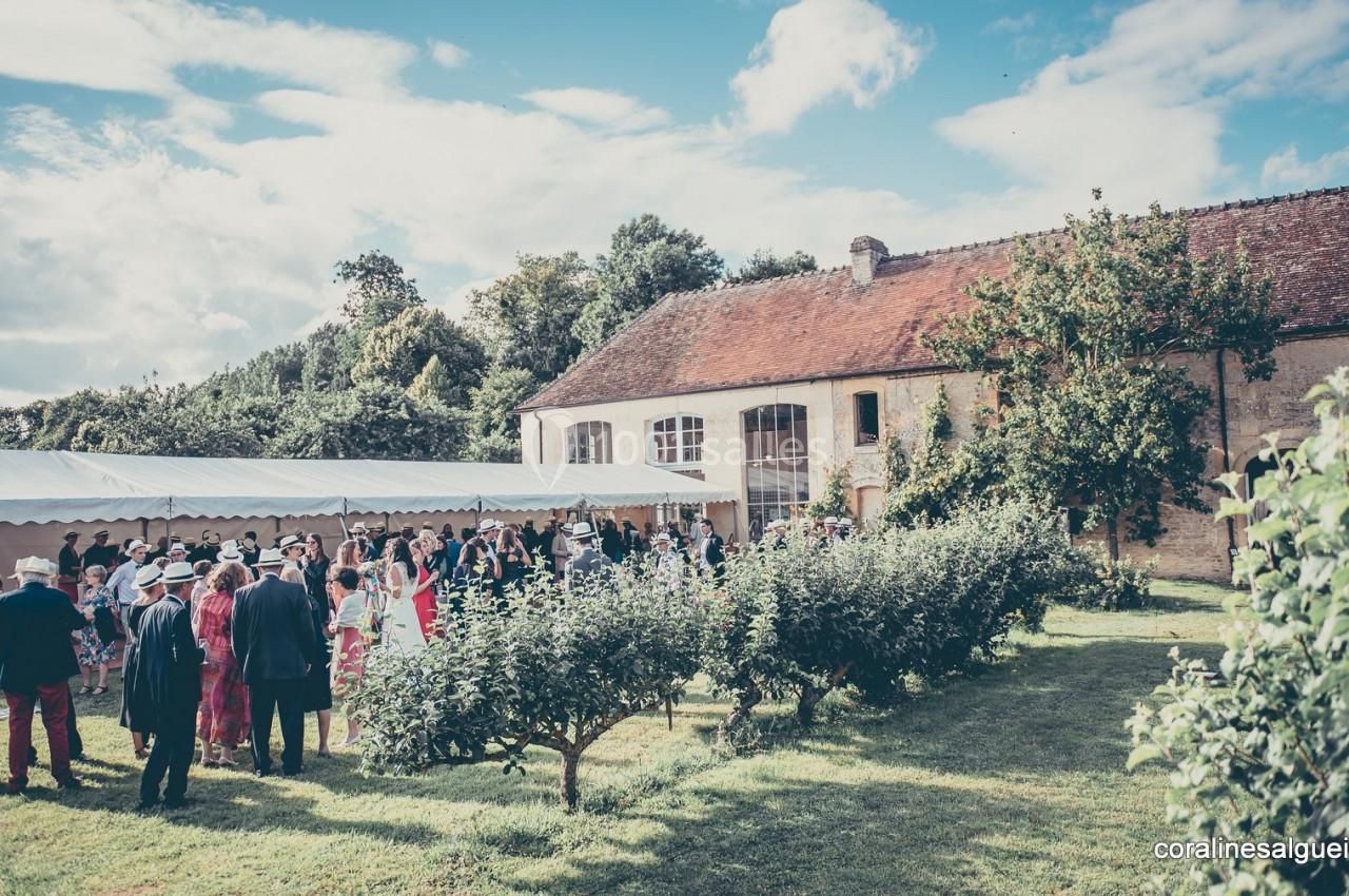 Groupe de personnes rassemblées dans un jardin près d'une bâtisse ancienne, sous une tente blanche par temps clair.