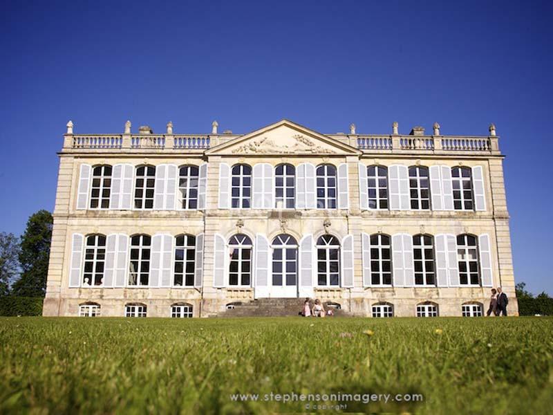 Façade d'un bâtiment historique avec de grandes fenêtres, entouré d'une pelouse sous un ciel bleu.