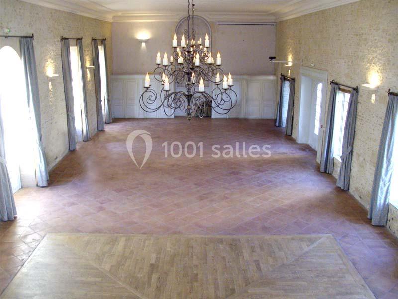 Salle spacieuse avec sol en terre cuite, parquet en avant-plan, murs clairs et grand lustre central suspendu.