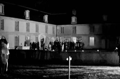 Groupe de personnes rassemblées dans un jardin près d'une bâtisse ancienne, sous une tente blanche par temps clair.