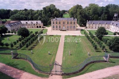 Groupe de personnes rassemblées dans un jardin près d'une bâtisse ancienne, sous une tente blanche par temps clair.