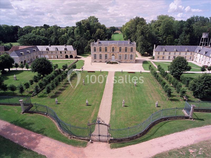 Vue aérienne d'un château entouré de jardins symétriques, avec des allées, des statues et des bâtiments annexes.