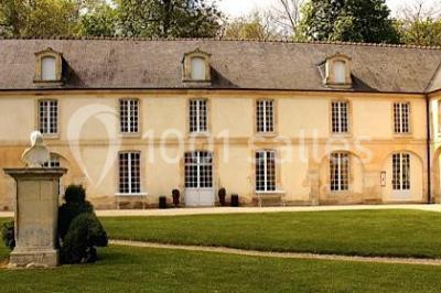 Groupe de personnes rassemblées dans un jardin près d'une bâtisse ancienne, sous une tente blanche par temps clair.