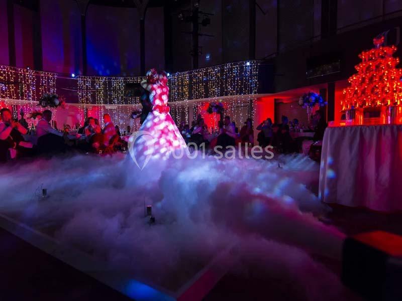 Une mariée danse au milieu d'une piste entourée de fumée et d'éclairages colorés dans une salle décorée.