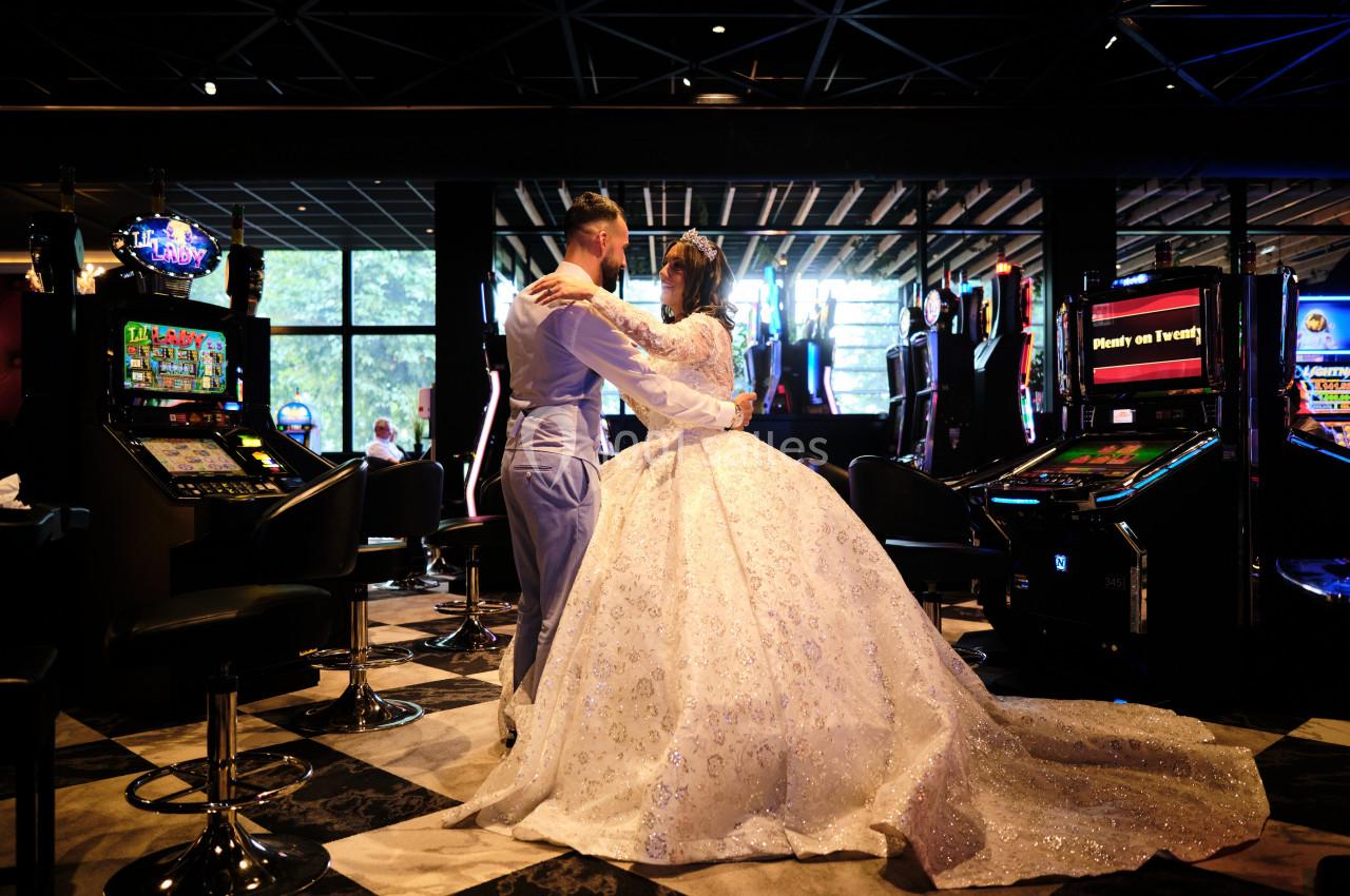 Un couple en tenue de mariage danse au milieu d'une salle de casino entourée de machines à sous.