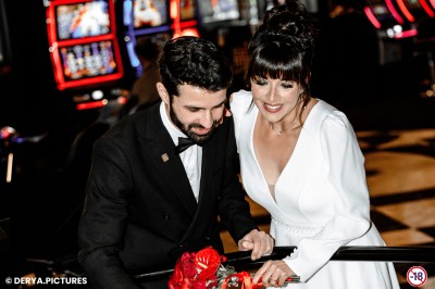 Un couple en tenue de mariage danse au milieu d'une salle de casino entourée de machines à sous.