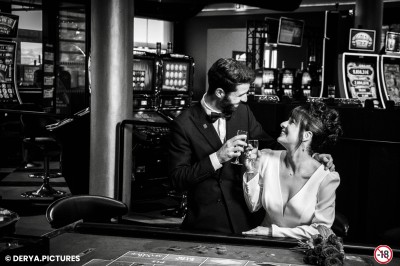 Un couple en tenue de mariage danse au milieu d'une salle de casino entourée de machines à sous.