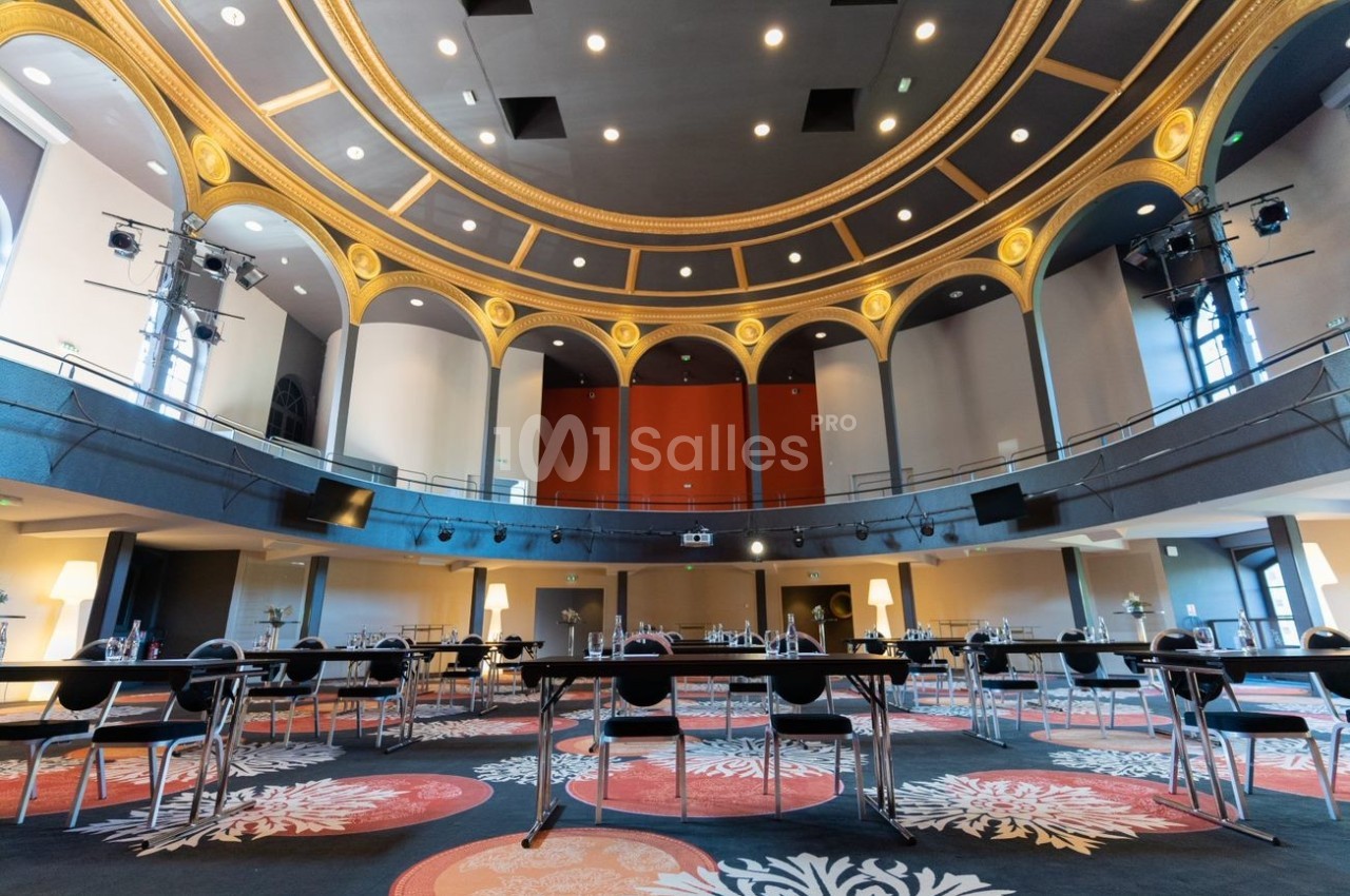 Salle de conférence circulaire avec plafond orné, tables et chaises disposées pour une réunion.