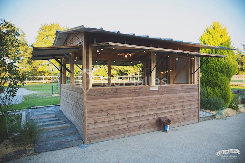 Kiosque en bois avec toit métallique, ouvert sur les côtés, situé dans un environnement extérieur verdoyant.