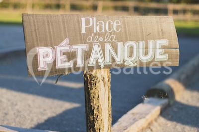 Vue d'une grange en bois entourée d'arbres, avec des bancs disposés en extérieur sur une pelouse.