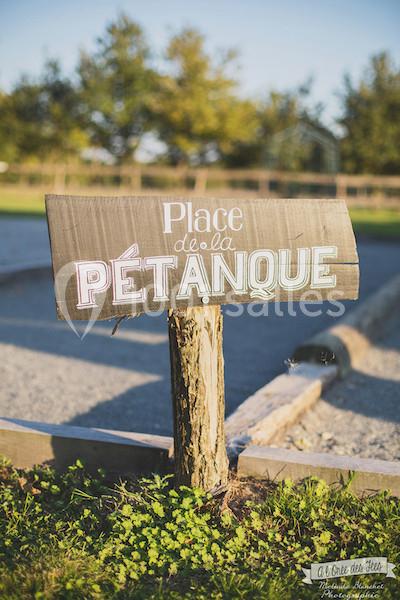 Panneau en bois indiquant ’Place de la pétanque’ devant un terrain de pétanque en plein air.