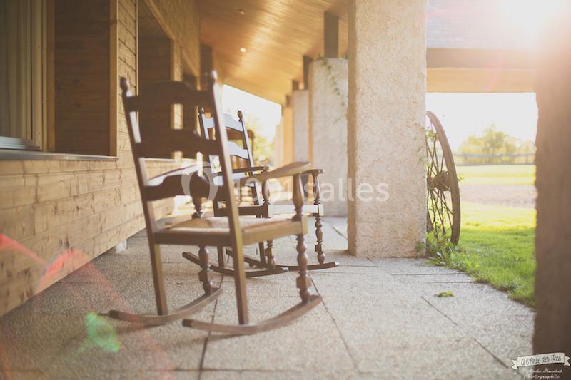 Deux chaises à bascule en bois sur une terrasse ensoleillée, avec vue sur un jardin verdoyant.