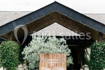 Vue d'une grange en bois entourée d'arbres, avec des bancs disposés en extérieur sur une pelouse.
