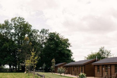 Vue d'une grange en bois entourée d'arbres, avec des bancs disposés en extérieur sur une pelouse.