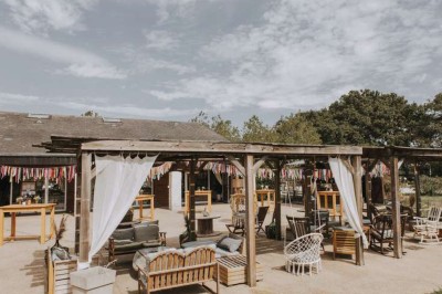 Vue d'une grange en bois entourée d'arbres, avec des bancs disposés en extérieur sur une pelouse.