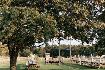 Vue d'une grange en bois entourée d'arbres, avec des bancs disposés en extérieur sur une pelouse.