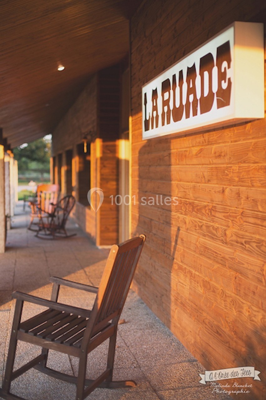 Façade en bois d'un bâtiment avec une enseigne ’La Ruade’ et des chaises en bois sur une terrasse ensoleillée.