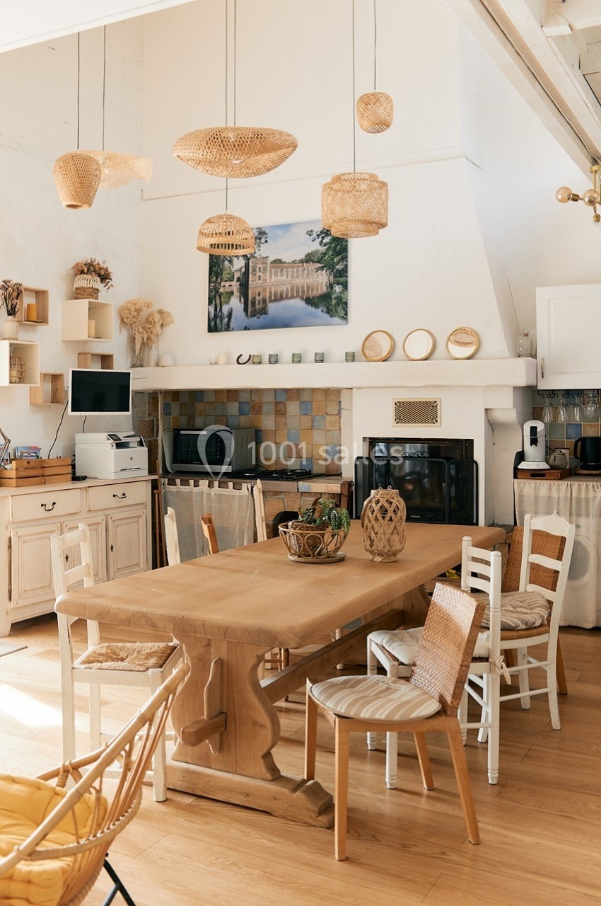 Cuisine lumineuse avec table en bois, chaises en osier, étagères décoratives et luminaires suspendus en rotin.