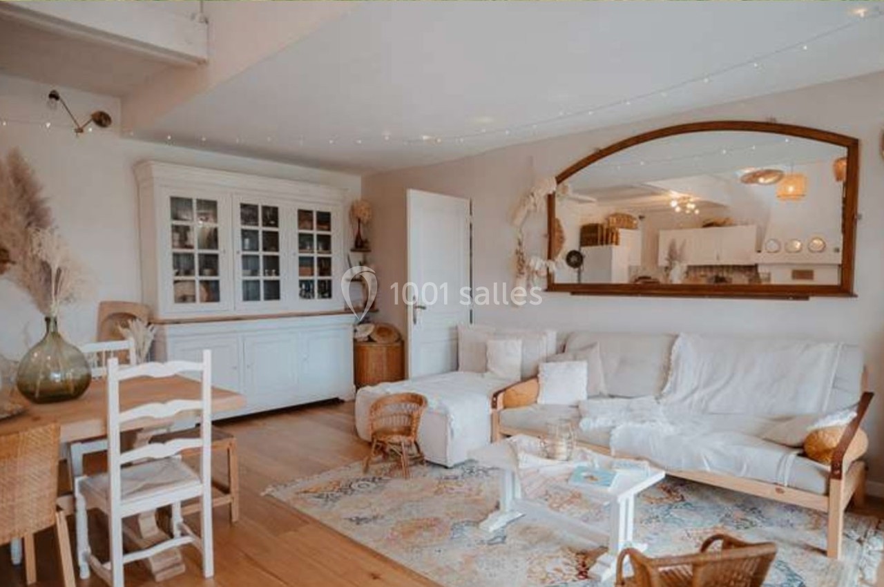 Salon lumineux avec canapé blanc, table basse, buffet vitré, miroir mural et décoration naturelle en bois et rotin.