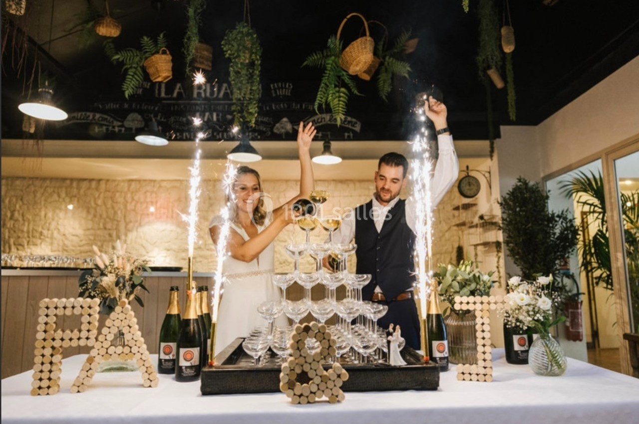 Un couple célèbre en versant du champagne sur une pyramide de verres, entouré de décorations festives.