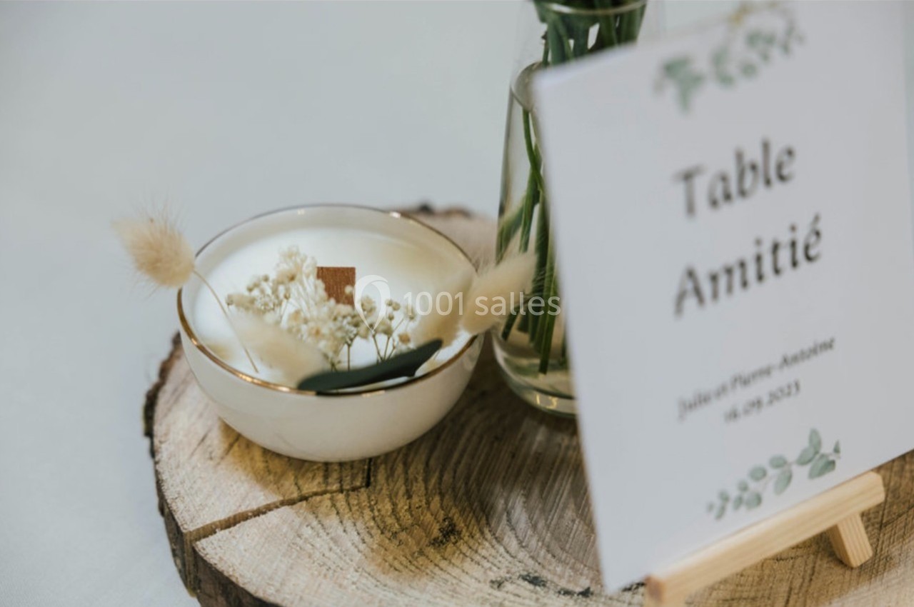 Centre de table avec fleurs séchées dans un bol en céramique et une carte indiquant ’Table Amitié’ sur une rondelle de bois.