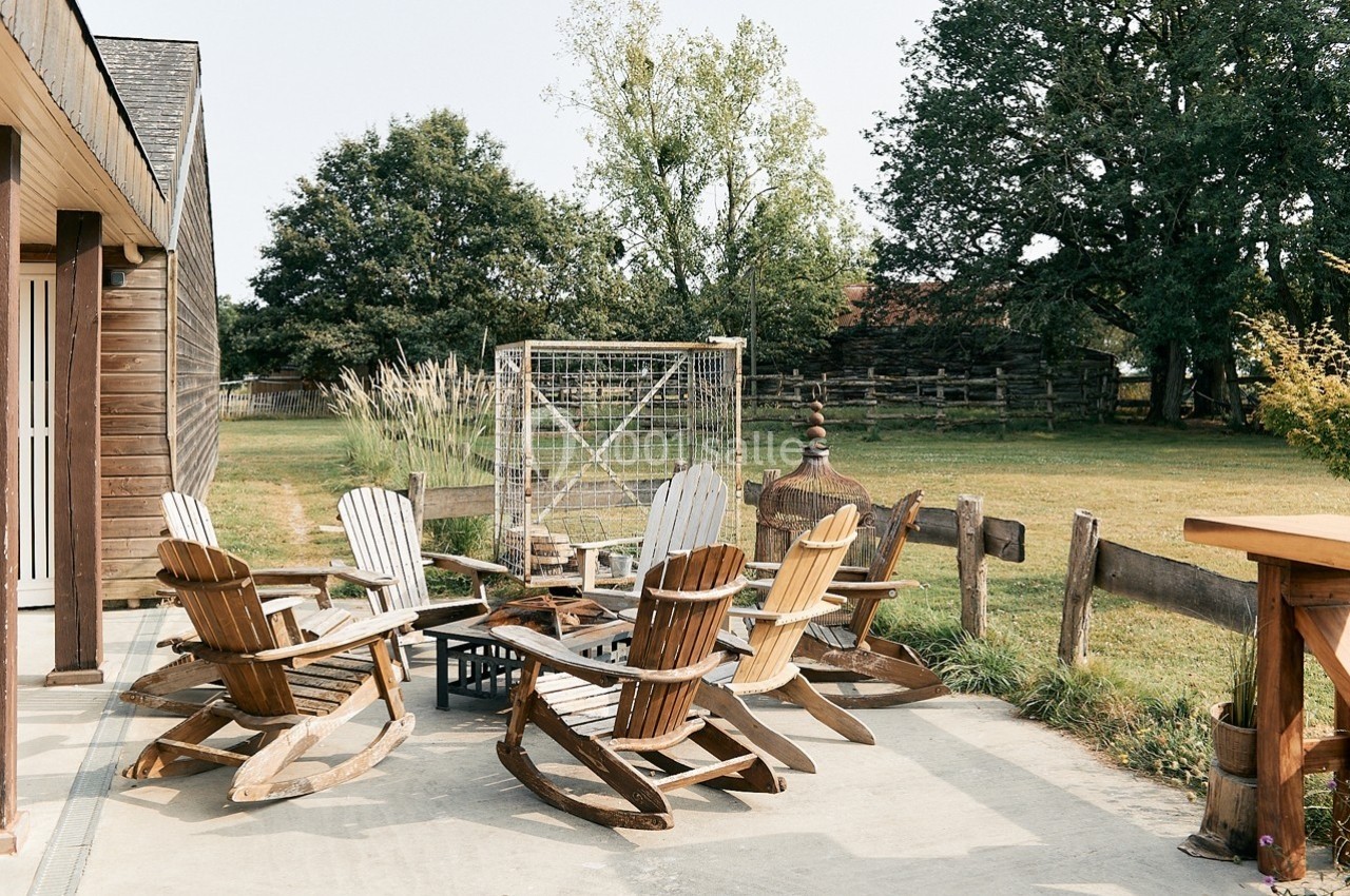 Chaises à bascule en bois disposées autour d'un foyer sur une terrasse, avec un jardin et des arbres en arrière-plan.